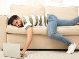 Fauler junger Mann liegt zuhause auf dem Sofa mit Laptop.