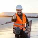 Ein glücklicher Arbeiter mit Bohrmaschine in den Händen gibt Daumen hoch für die Verwendung von Sonnenkollektoren.