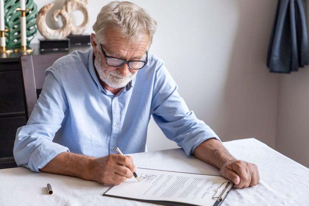 Aelterer Mann unterzeichnet ein handschriftliches Testament am Tisch – Symbolbild fuer Erbrecht Wuerzburg